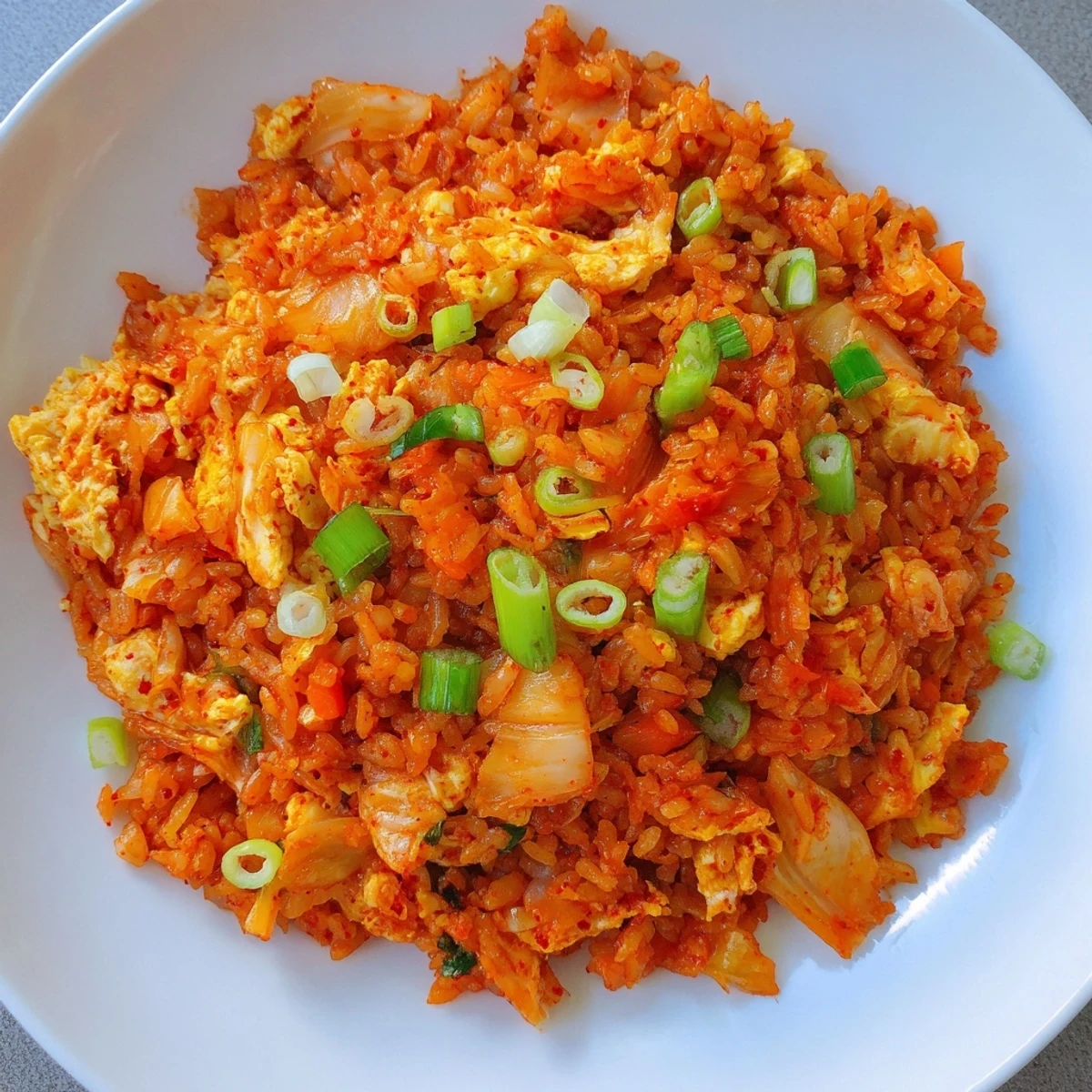 Steaming bowl of Spicy Kimchi Fried Rice topped with sesame seeds and green onions, served with a side of kimchi.