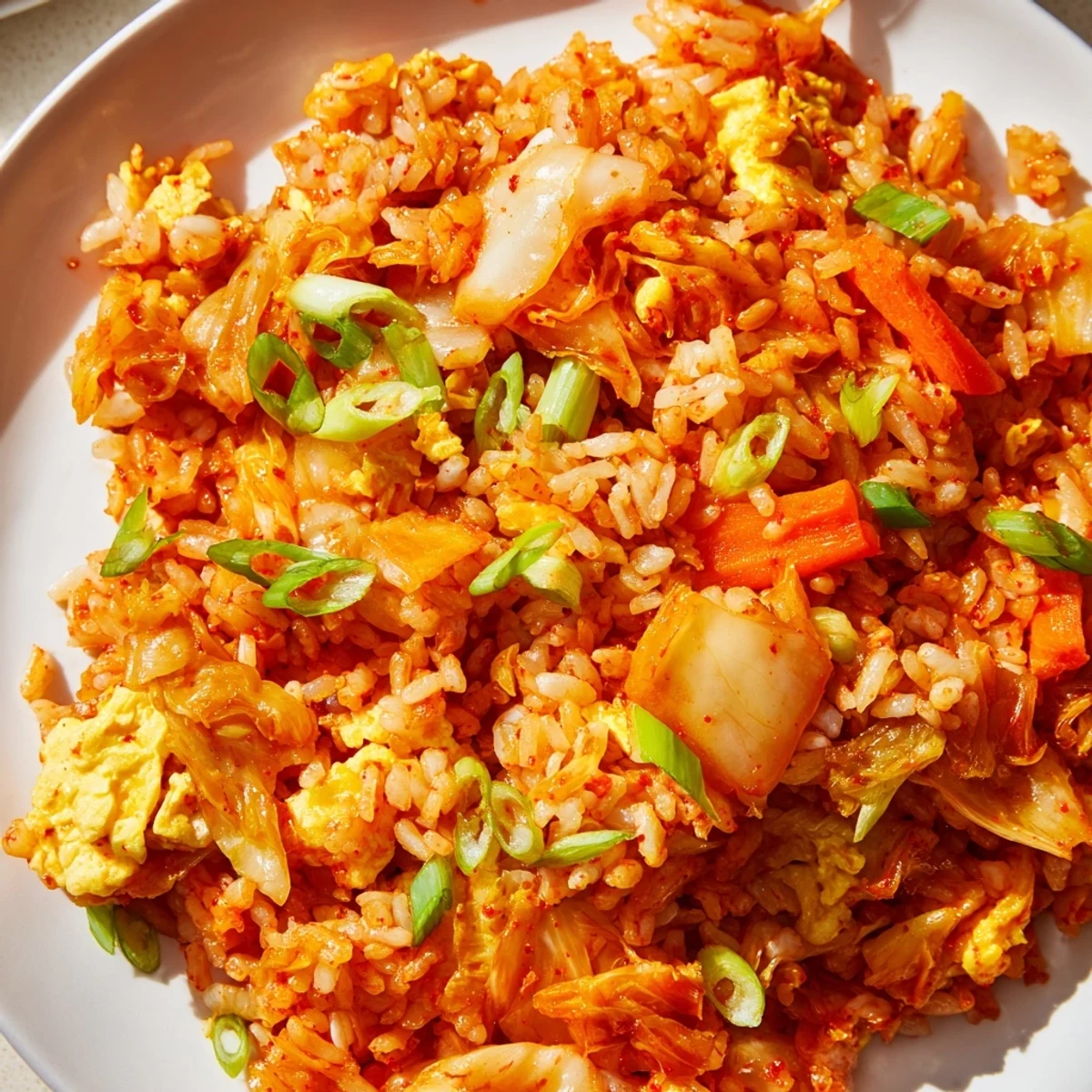 Golden-brown Spicy Kimchi Fried Rice with sautéed vegetables, garnished with roasted seaweed strips on a rustic table.