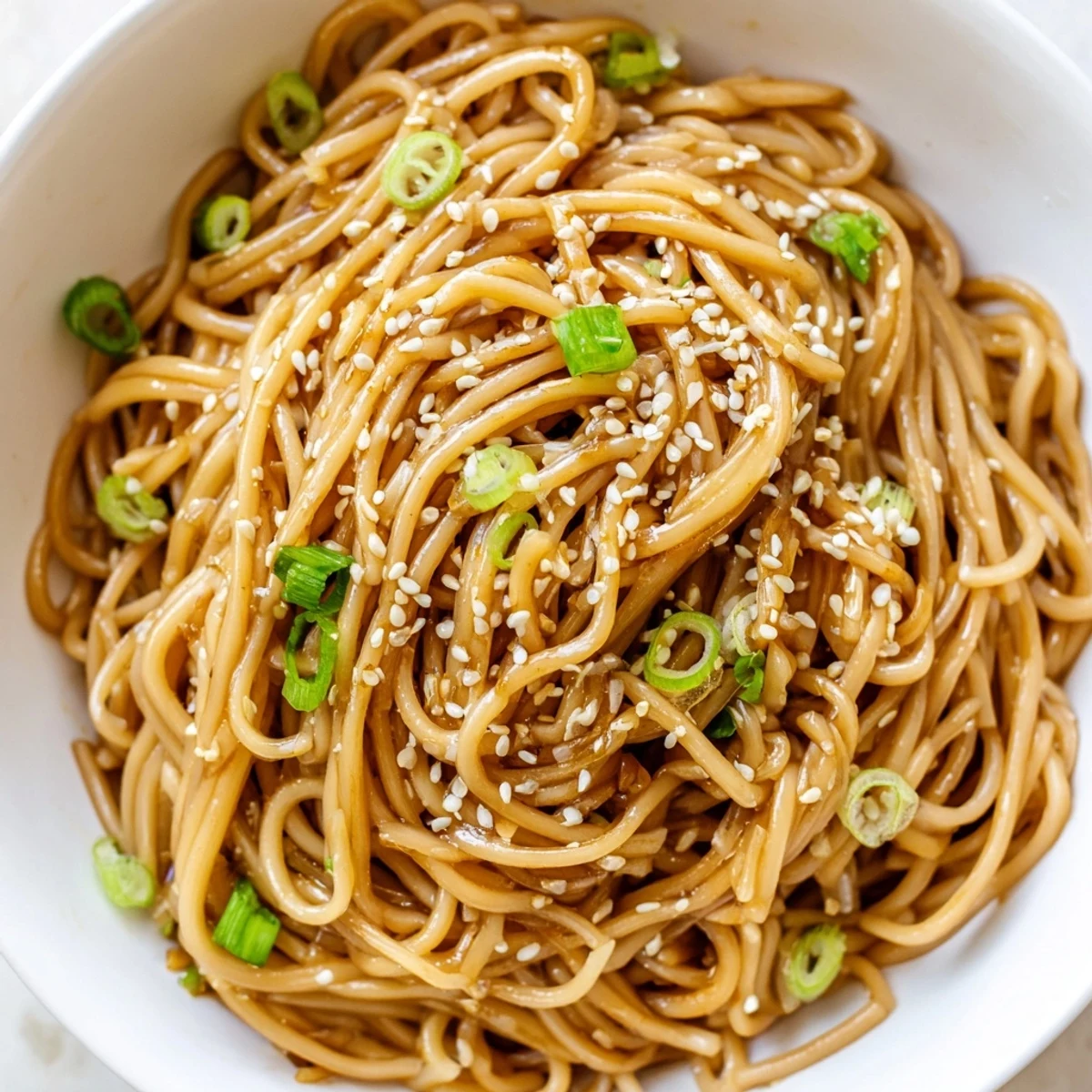 Tossed noodles in a glossy garlic-butter sauce, garnished with sesame seeds and green onions for a quick Asian garlic noodle bowl.  