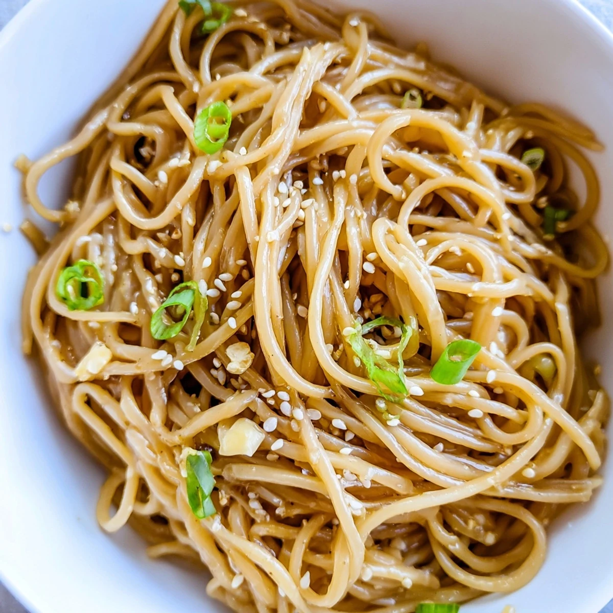 A fork lifts tender noodles from an Asian garlic noodle bowl, showcasing rich soy sauce glaze and fresh cilantro garnish.