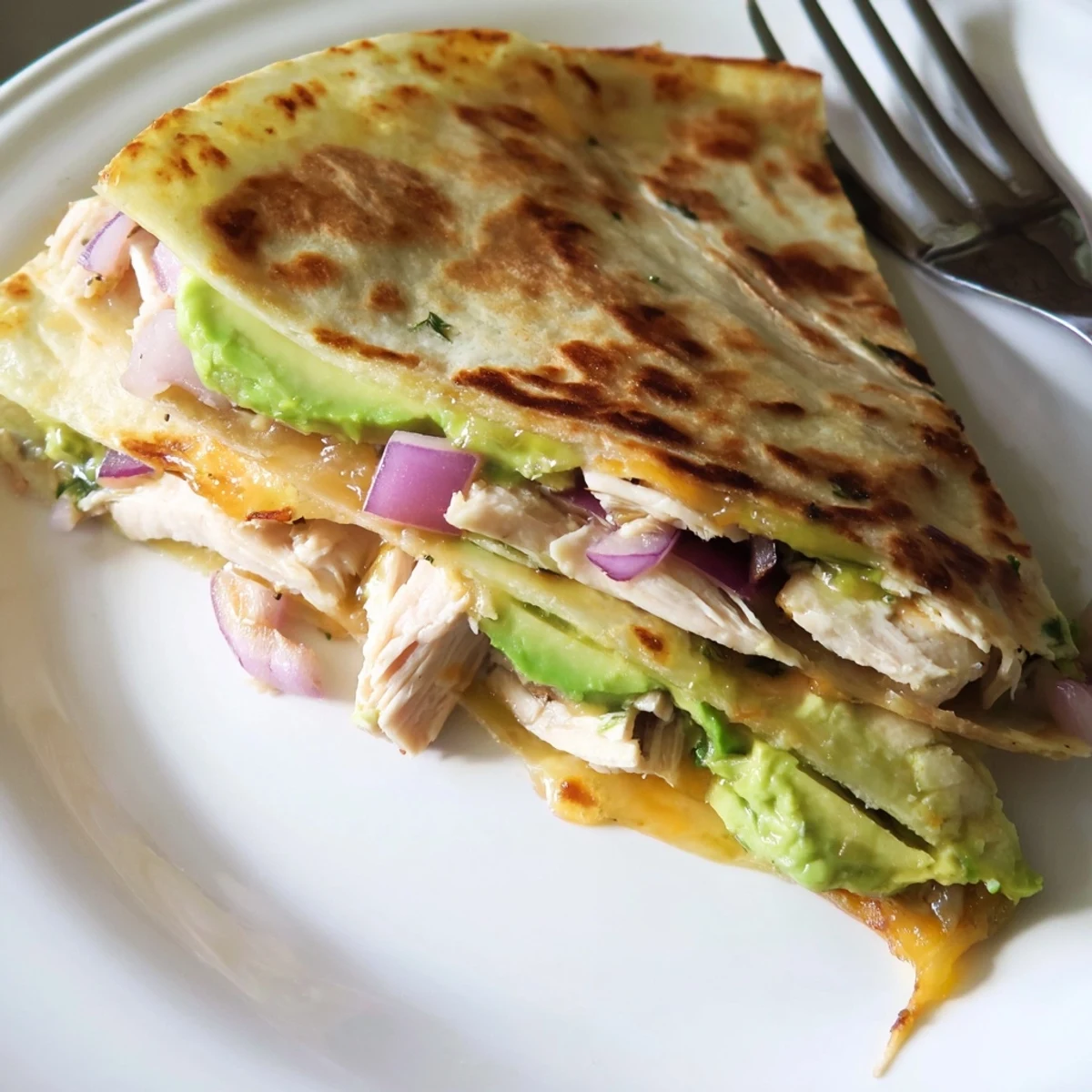 Crispy golden Chicken Avocado Quesadilla wedges showcasing melted cheese, grilled chicken, and fresh avocado slices on a plate.  