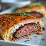 Sliced Beef Wellington revealing juicy pink beef, mushroom duxelles, and prosciutto layers.