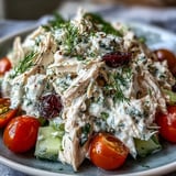 A spoon scoops creamy Tzatziki Chicken Salad loaded with shredded rotisserie chicken, cherry tomatoes, and feta cheese.