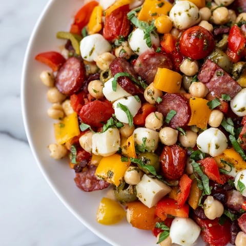 A close-up of a vibrant Crunchy Antipasto Chopped Salad loaded with chickpeas, diced salami, and mozzarella pearls in zesty Italian dressing.
