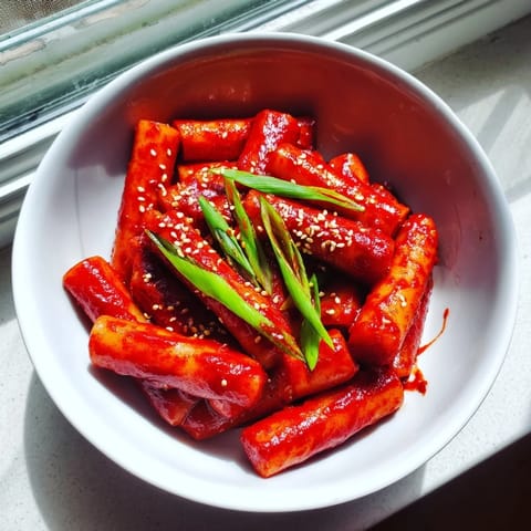 Close-up of Korean Tteokbokki in a skillet, garnished with sesame seeds and sliced onions, ready to serve.