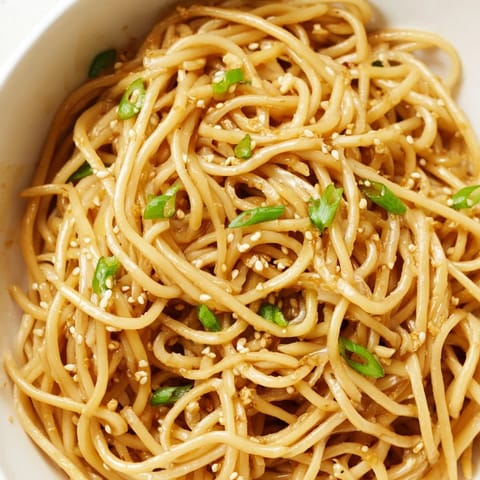 A close-up of steaming Asian garlic noodle bowl with chili slices and julienned carrots on top, ready to serve.  
