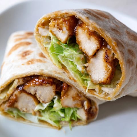 A sliced Honey Mustard Chicken Wrap revealing layers of juicy chicken, fresh romaine, and vibrant red onion on a plate.