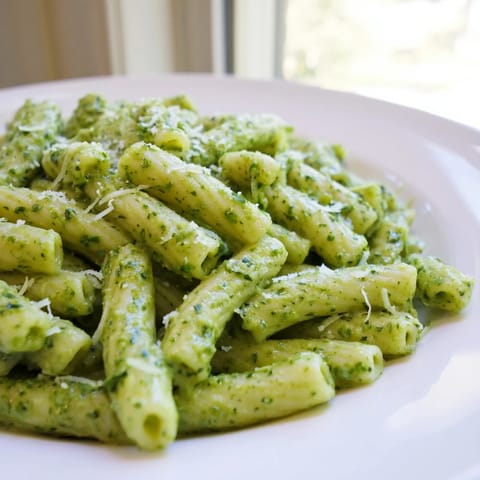 Steaming Creamy Avocado Pesto Mac with bright green basil leaves and a lemon wedge on the side, ready to serve.