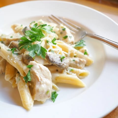 Fresh parsley and grated Parmesan garnish a plate of Roasted Garlic Chicken Penne, served with a crisp green salad on the side.
