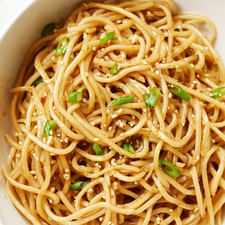 A close-up of steaming Asian garlic noodle bowl with chili slices and julienned carrots on top, ready to serve.  