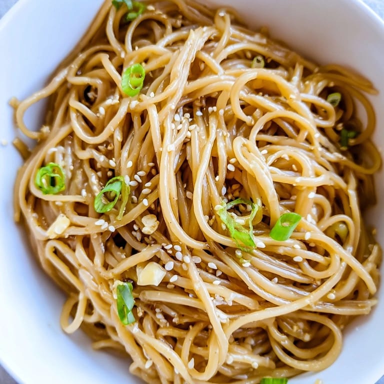A fork lifts tender noodles from an Asian garlic noodle bowl, showcasing rich soy sauce glaze and fresh cilantro garnish.