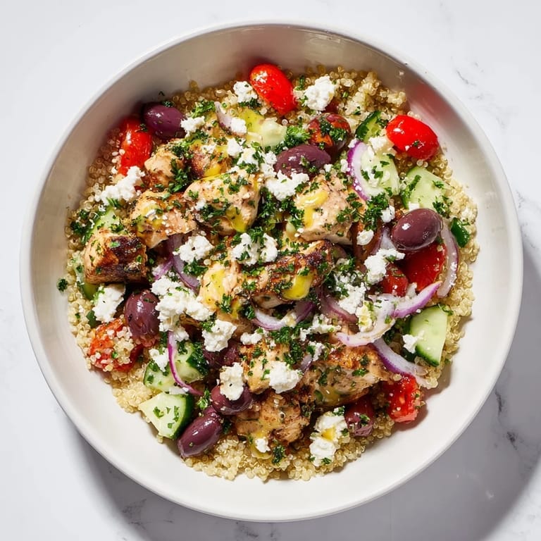 A close-up of a Mediterranean Chicken Bowl with tangy Kalamata olives, cherry tomatoes, red onion, chickpeas, creamy feta, and a bright zesty dressing.  