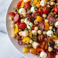 A close-up of a vibrant Crunchy Antipasto Chopped Salad loaded with chickpeas, diced salami, and mozzarella pearls in zesty Italian dressing.